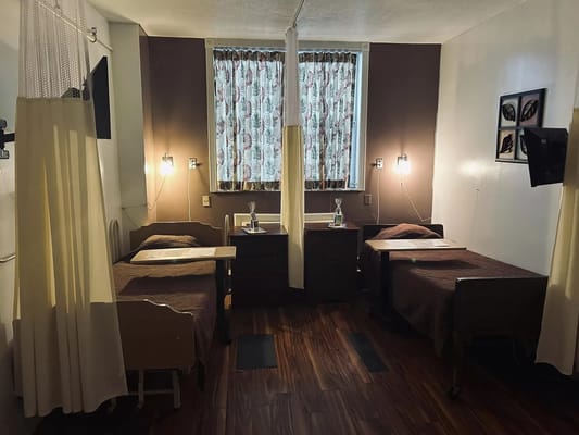 A well-lit patient room with two beds, curtains, and a window.