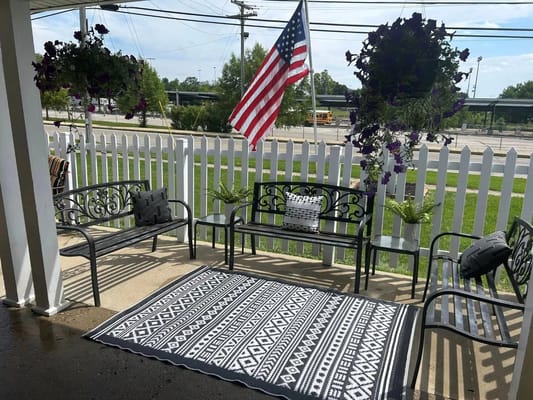 A welcoming porch with benches, a patterned rug, and hanging plants