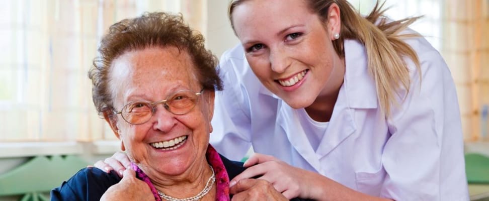 A caregiver and a resident smiling together in a facility.