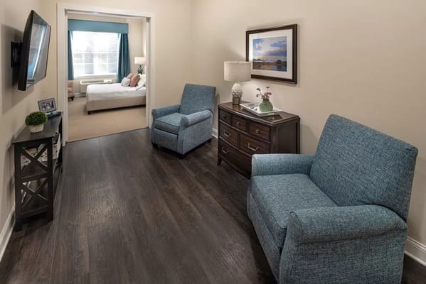 Cozy living area featuring two blue armchairs and a dresser in a senior living facility.