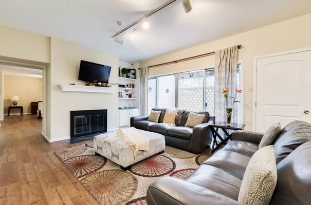 A cozy living room with a fireplace, television, and large windows