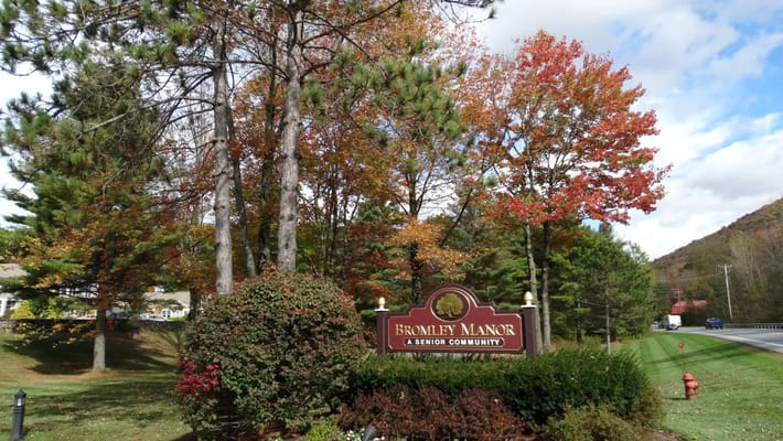 Entrance sign for Bromley Manor Senior Community amid autumn trees