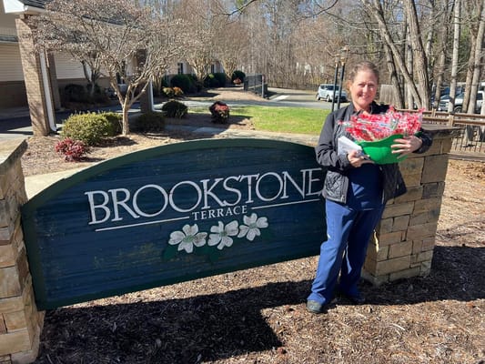 Staff member holding a basket of flowers at the Brookstone Terrace sign.