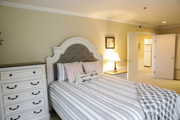 A cozy bedroom featuring a striped bedspread, decorative pillows, and a dresser.