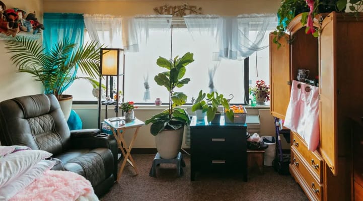 Interior of a senior living room with plants, a chair, and a closet.