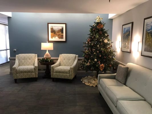 A decorated lobby with light blue walls, two chairs, a lamp, and a Christmas tree.