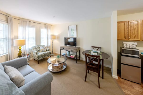 Living room with a sofa, armchair, dining table, and kitchenette.