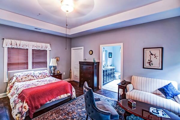 A cozy bedroom featuring a bed, dresser, and seating area.