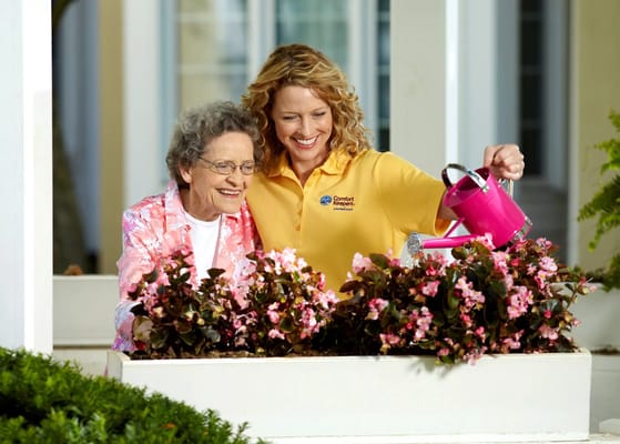 Senior resident and caregiver watering flowers in a garden