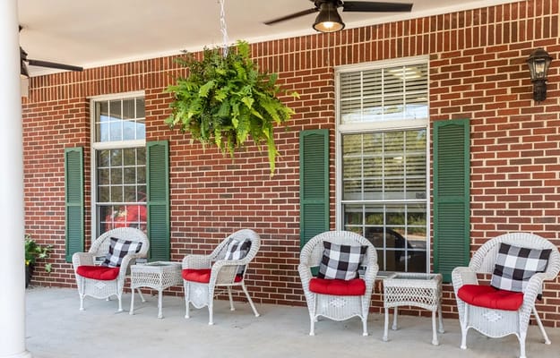 White wicker chairs with red cushions and a hanging fern on a patio