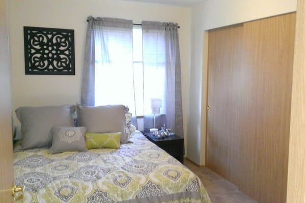 A cozy bedroom featuring a bed with decorative pillows and a window with light curtains.