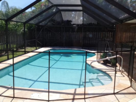 In-ground pool surrounded by a safety fence under a screened enclosure