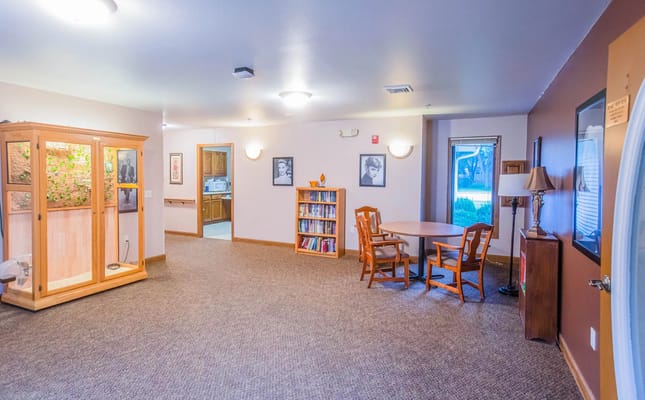 A spacious common area with a table, chairs, bookshelves, and decorative elements.