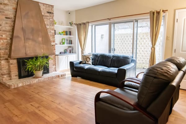 Spacious living room featuring a black leather sofa and a stone fireplace