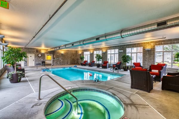 Indoor pool and hot tub surrounded by seating areas.