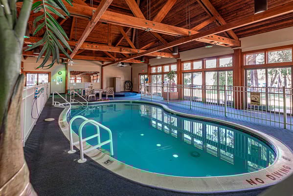 View of the indoor pool at Complete Care at Silverwoods with wooden beams and seating area.