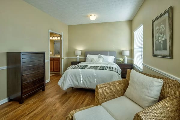 Comfortable bedroom with a bed, dresser, and seating area in senior living facility.