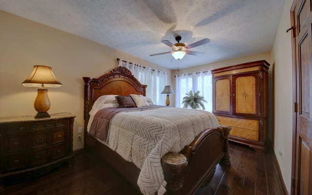A cozy bedroom featuring a wooden bed, a lamp, and furnishings.