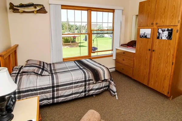 A well-furnished bedroom featuring a bed, lamp, and wardrobe with a view of the outdoors