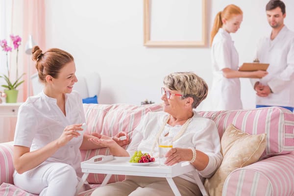 Caregiver assisting a resident with medication in a homey lounge.