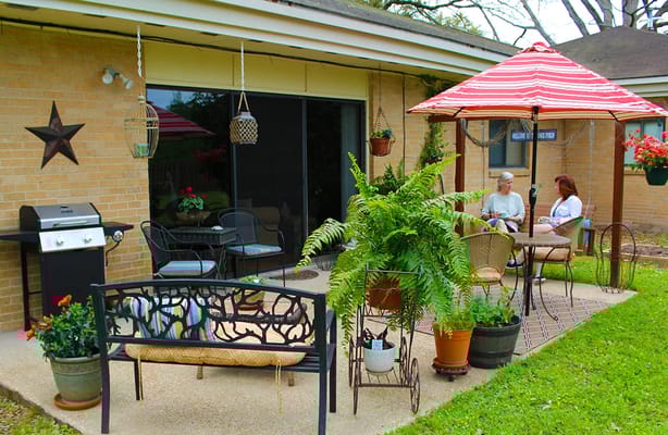 Two residents enjoying tea on the patio surrounded by plants and a grill.