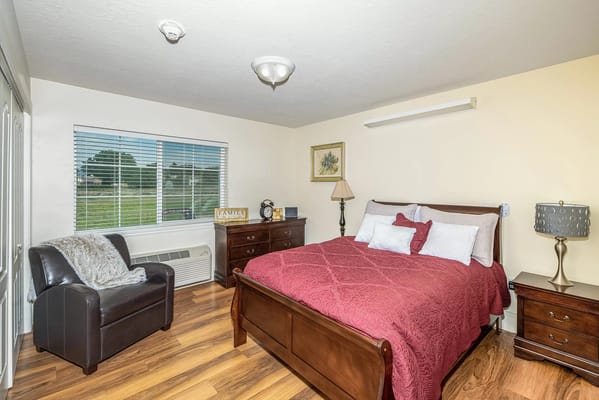 A cozy bedroom featuring a bed, dresser, and armchair.