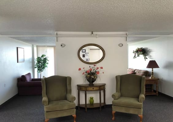 A cozy seating area featuring two green armchairs and a small table with a decorative vase.