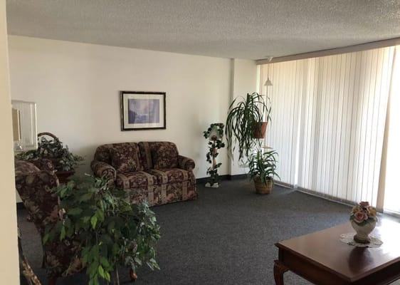 A cozy living room with floral sofas and potted plants.