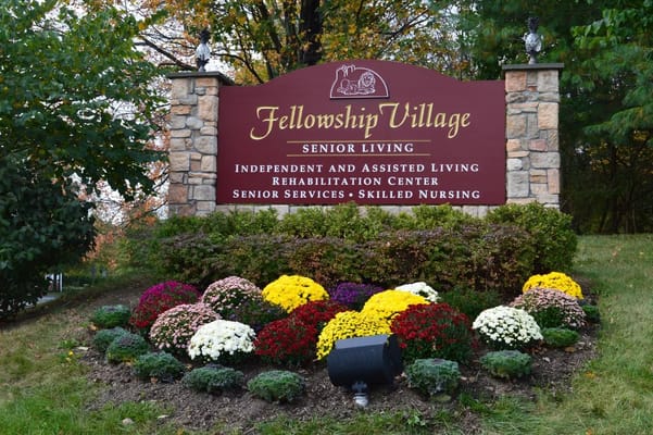 Sign for Fellowship Village senior living facility with colorful flower beds.