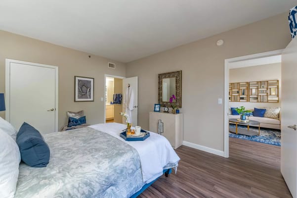 A spacious bedroom with a bed, decorative pillows, and a view into the living area.