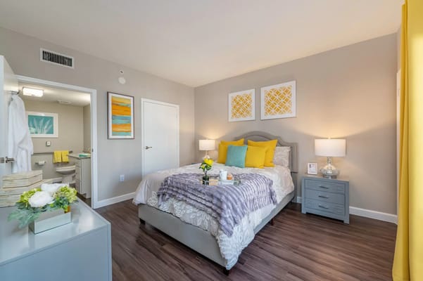 A cozy bedroom featuring a bed with colorful pillows and a bright yellow curtain.