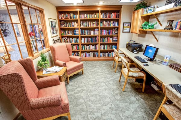 A comfortable library corner with armchairs, a bookshelf filled with books, and a workspace.