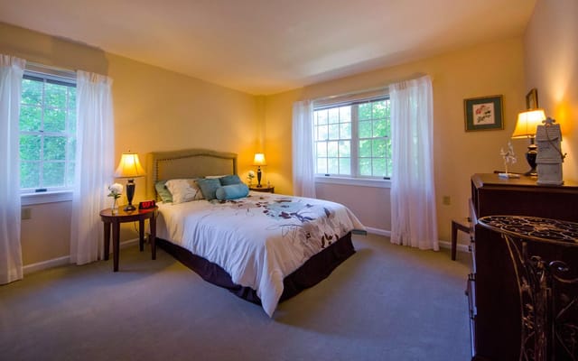 A cozy bedroom featuring a bed with floral bedding, nightstands with lamps, and a window with sheer curtains.