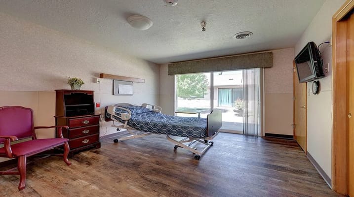 A resident room featuring an adjustable bed, a chair, and a TV.