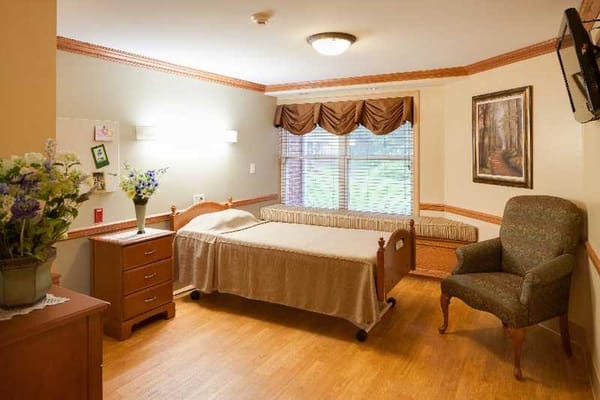 A stylishly furnished resident room featuring a bed, chair, and window with natural light.