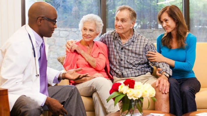 A doctor consulting with a senior couple and their daughter in a sunny room.