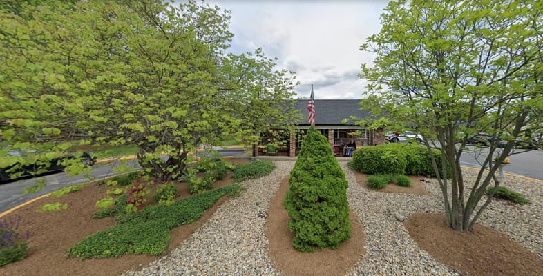 Gardens and entrance of Golden Living Center Bloomington with trees and an American flag.