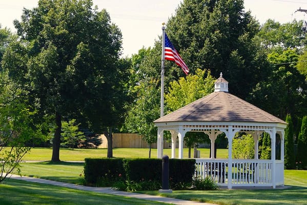 White gazebo surrounded by greenery and an American flag