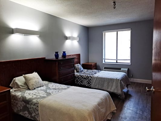 A well-lit bedroom with two beds, a dresser, and decorative vases.