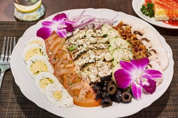 A colorful salad platter featuring sliced vegetables, chicken, and garnishes.
