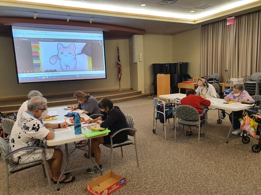 Seniors engaged in an art class with a drawing demonstration on a screen.