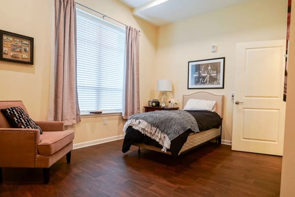 A comfortable bedroom featuring a bed, chair, and decorative lamp