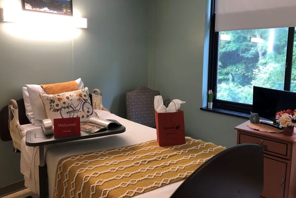 Spacious bedroom with hospital bed, decorative pillow, and welcome sign.