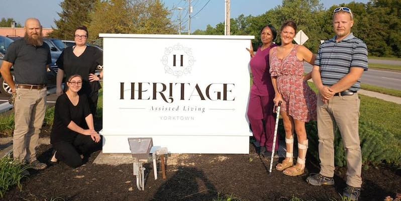 Staff and residents in front of Heritage Assisted Living sign