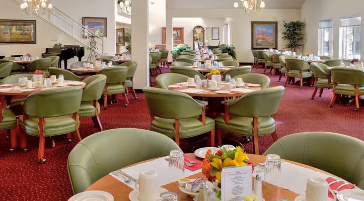 Spacious dining room with green chairs and tables set for meals.