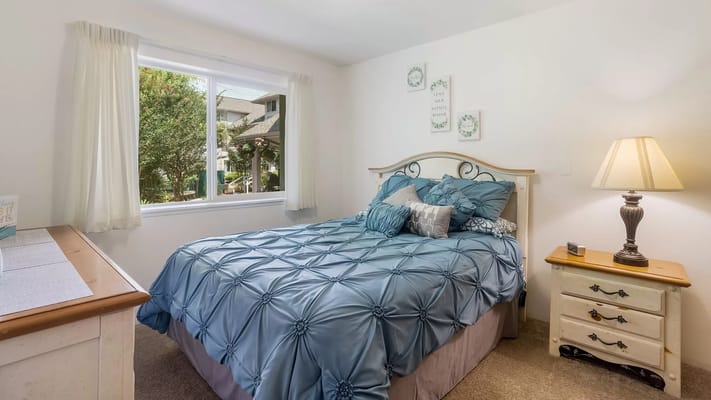 A well-decorated bedroom featuring a blue comforter and a window with a view.