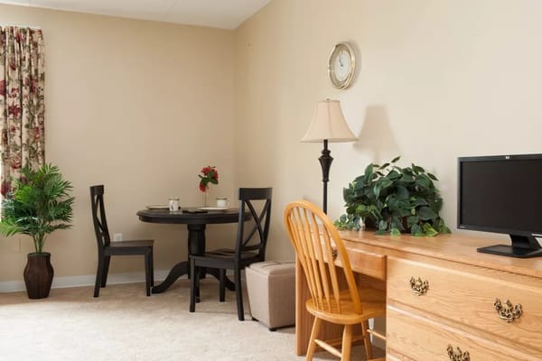 A cozy living area featuring a small dining table, a chair, and a desk with a television.