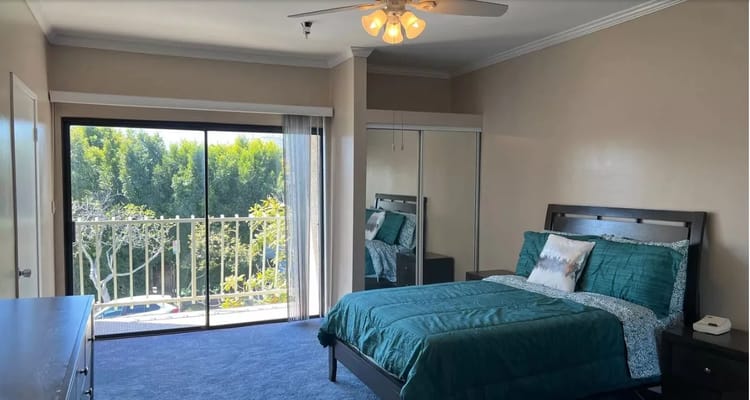 A bright bedroom featuring a queen-sized bed and a large window with a balcony view.