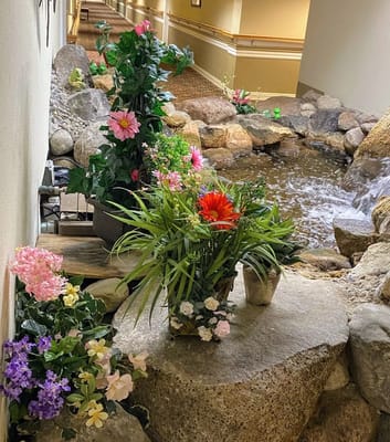 Vibrant flower arrangements near a stone water feature in a hallway.