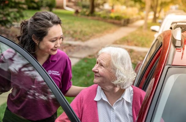 A caregiver helping a senior woman out of a car in a residential area
